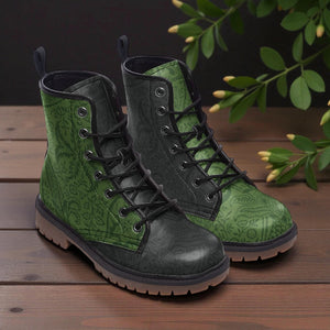 A pair of green patterned boots with black laces and soles, placed on a wooden surface with green leaves in the background.