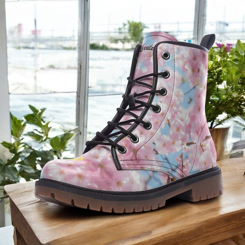 A pink and white floral patterned boot is displayed on a wooden surface, with a window and potted plants visible in the background.