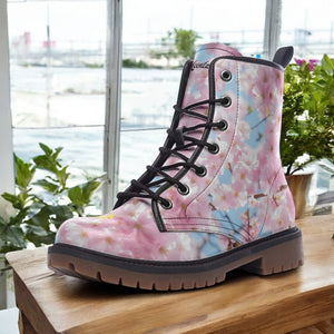 A pink and white floral patterned boot is displayed on a wooden surface, with a window and potted plants visible in the background.